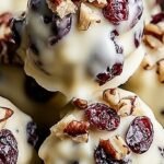 A pile of white chocolate clusters with pecans and red cranberries on parchment paper