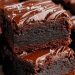 A stack of fudgy flourless brownies topped with melted chocolate chips on a wooden board.