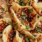 A small ceramic bowl filled with dark dumpling dipping sauce topped with green scallions and chili oil flakes.