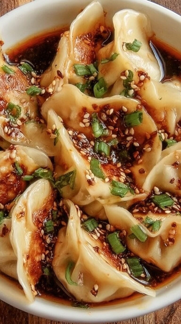 A small ceramic bowl filled with dark dumpling dipping sauce topped with green scallions and chili oil flakes.