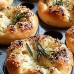 Golden brown individual focaccia muffins topped with fresh rosemary and sea salt in a muffin tin.