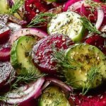 A colorful fresh cucumber and beetroot salad with green herbs in a glass bowl.