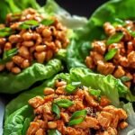 A platter of fresh butter lettuce leaves filled with savory ground chicken and drizzled with spicy Thai chili sauce.